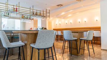 Un espace bar moderne avec des tabourets hauts, un comptoir en bois et un plafond décoratif agrémenté de luminaires suspendus.