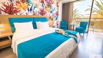 Quarto de hotel com uma cama grande, varanda e vista, além de parede com padrão de folhagem tropical.