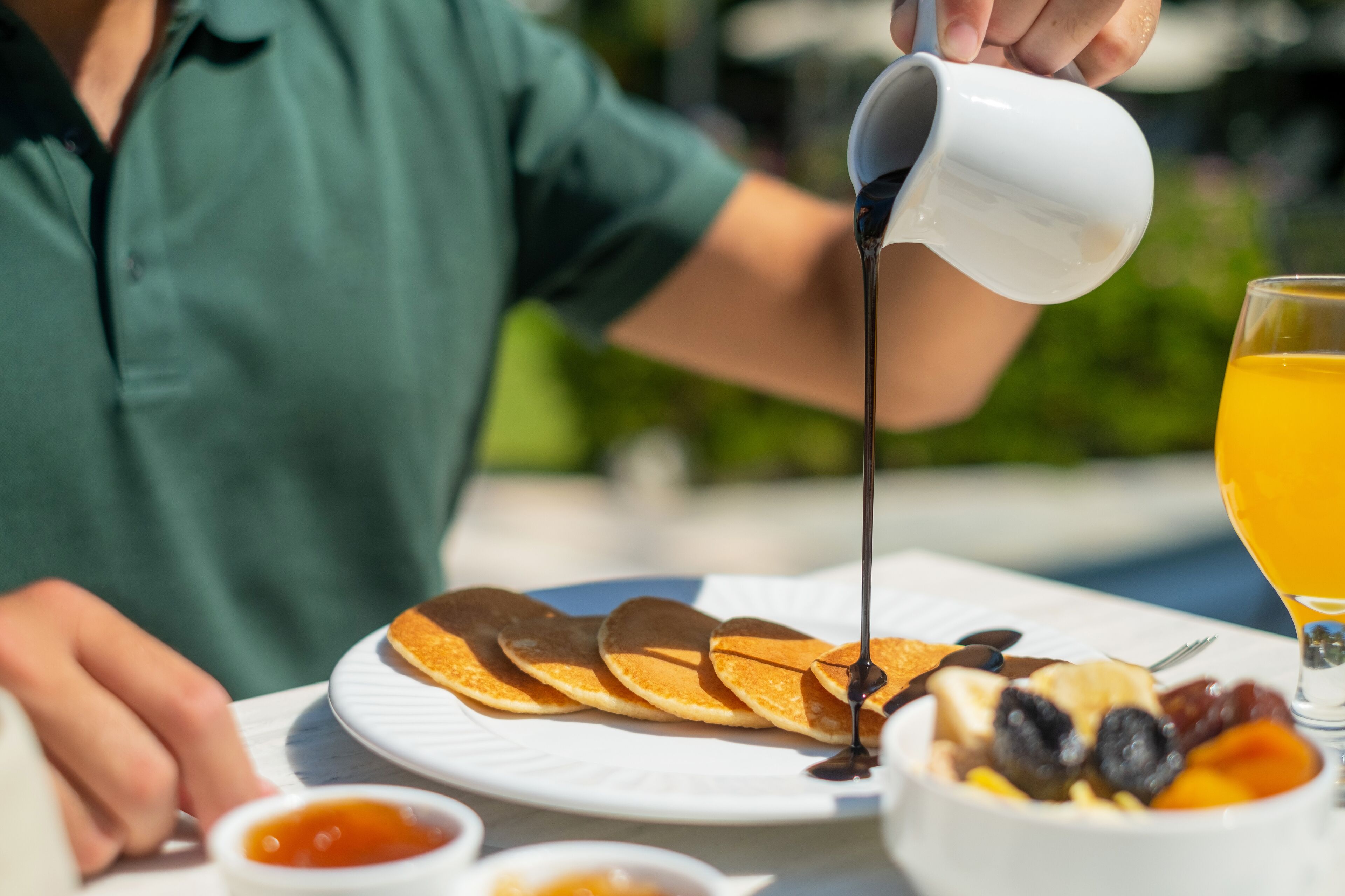 Een ontbijt met pannenkoeken, fruit en een glas sinaasappelsap op een tafel.