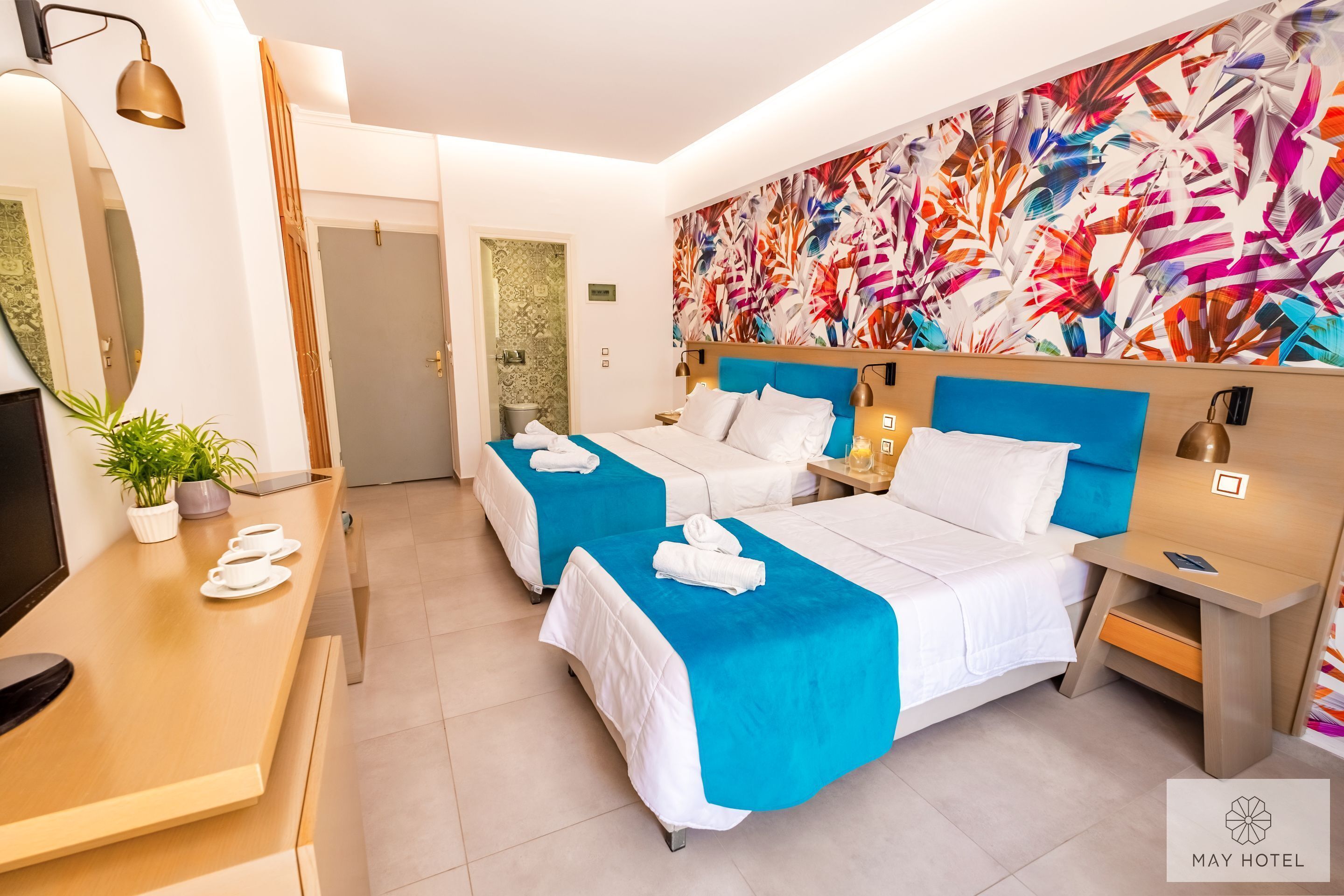 Une chambre d’hôtel avec deux lits, un bureau, une télévision et une fresque murale abstraite aux couleurs vives.