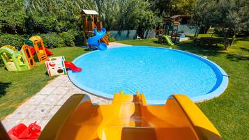 A swimming pool with slides and a play structure in a backyard.