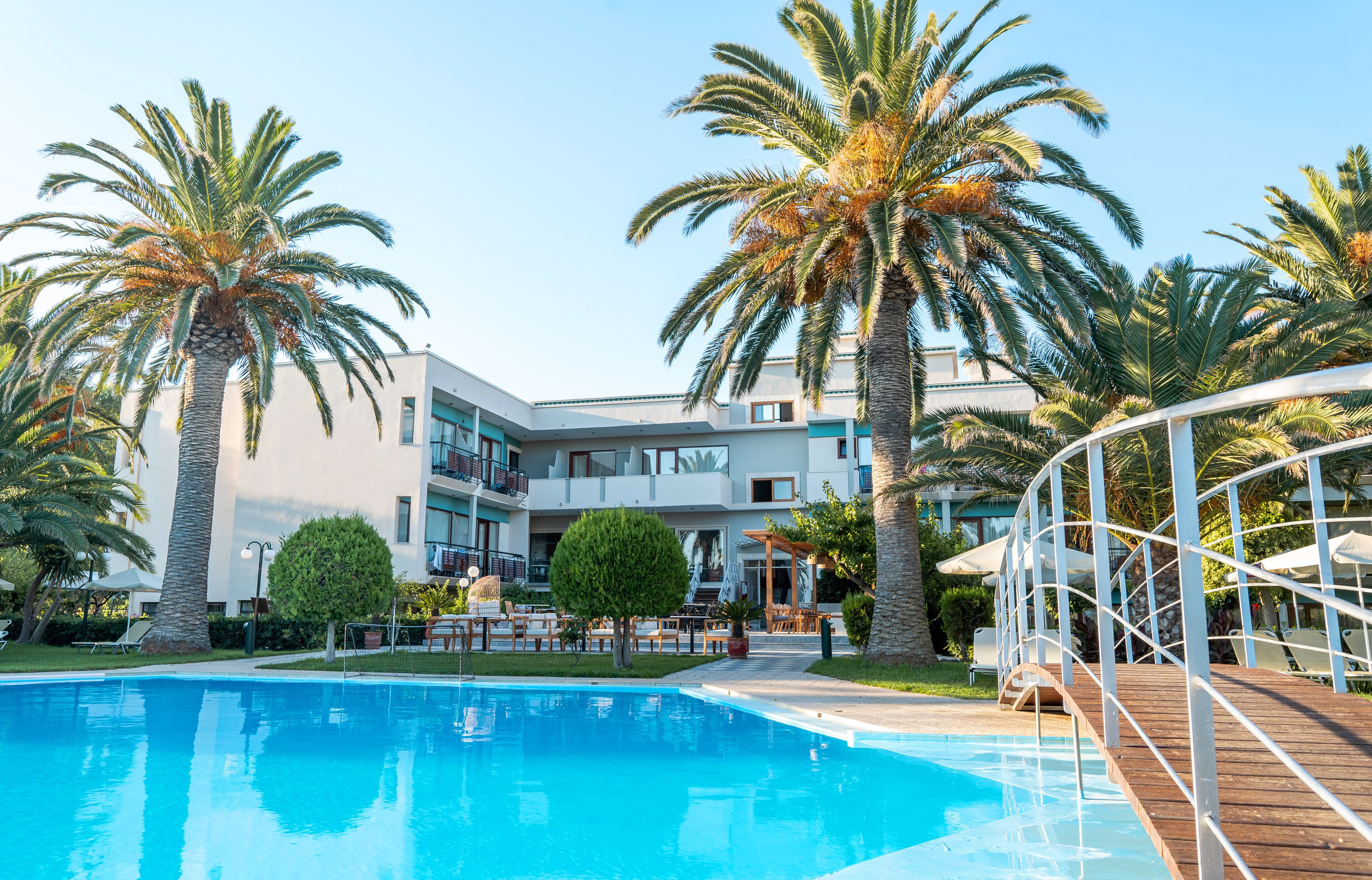 A pool area with palm trees, a wooden deck, and a building with balconies.
