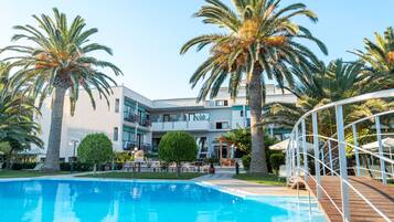 A pool area with palm trees, a wooden deck, and a building with balconies.