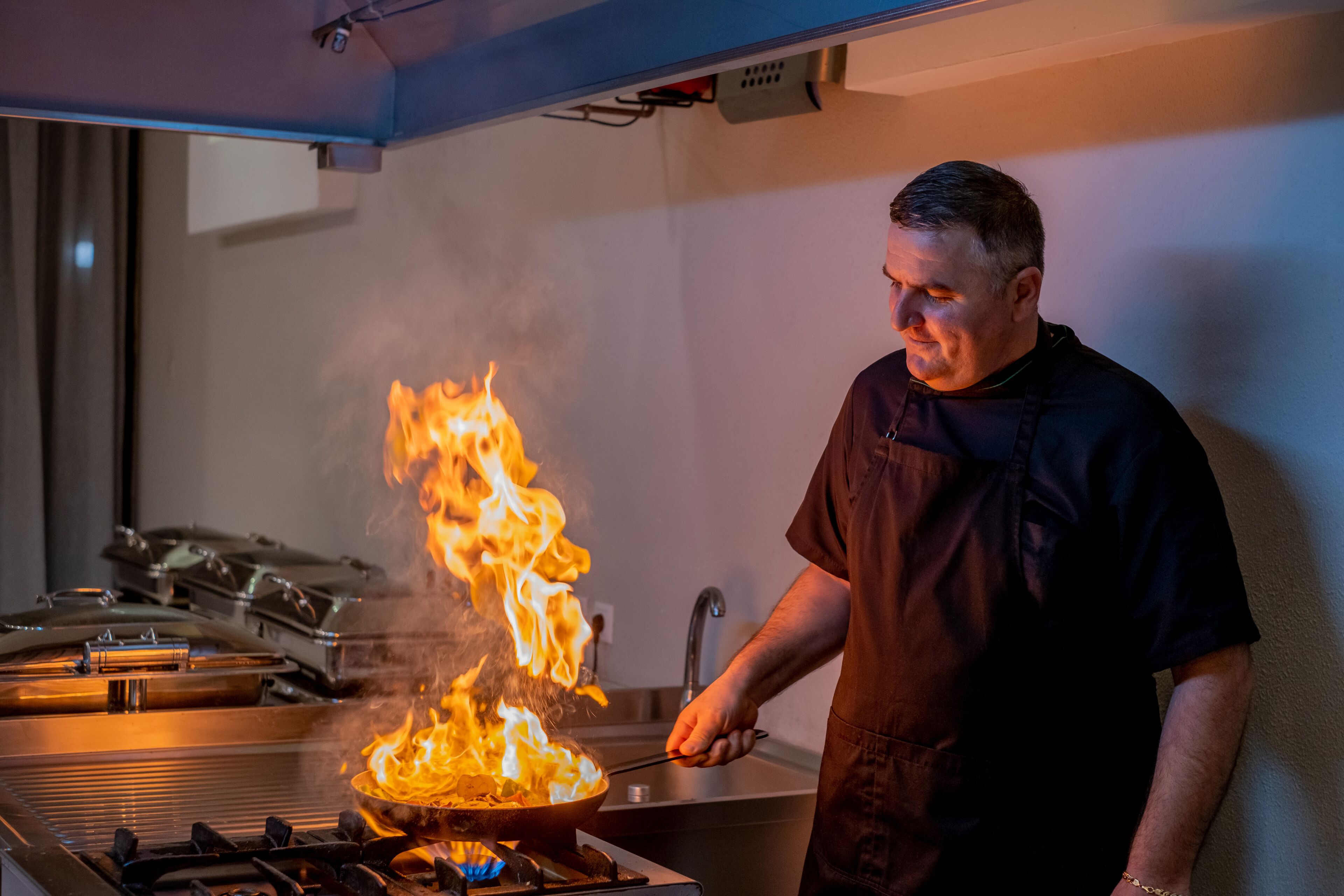 A chef cooking with flames on a stove in a kitchen.