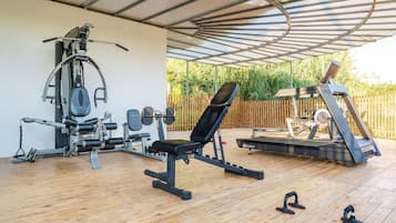 Un gimnasio al aire libre techado con equipo de ejercicios, incluyendo una banca, mancuernas y una cinta de correr.