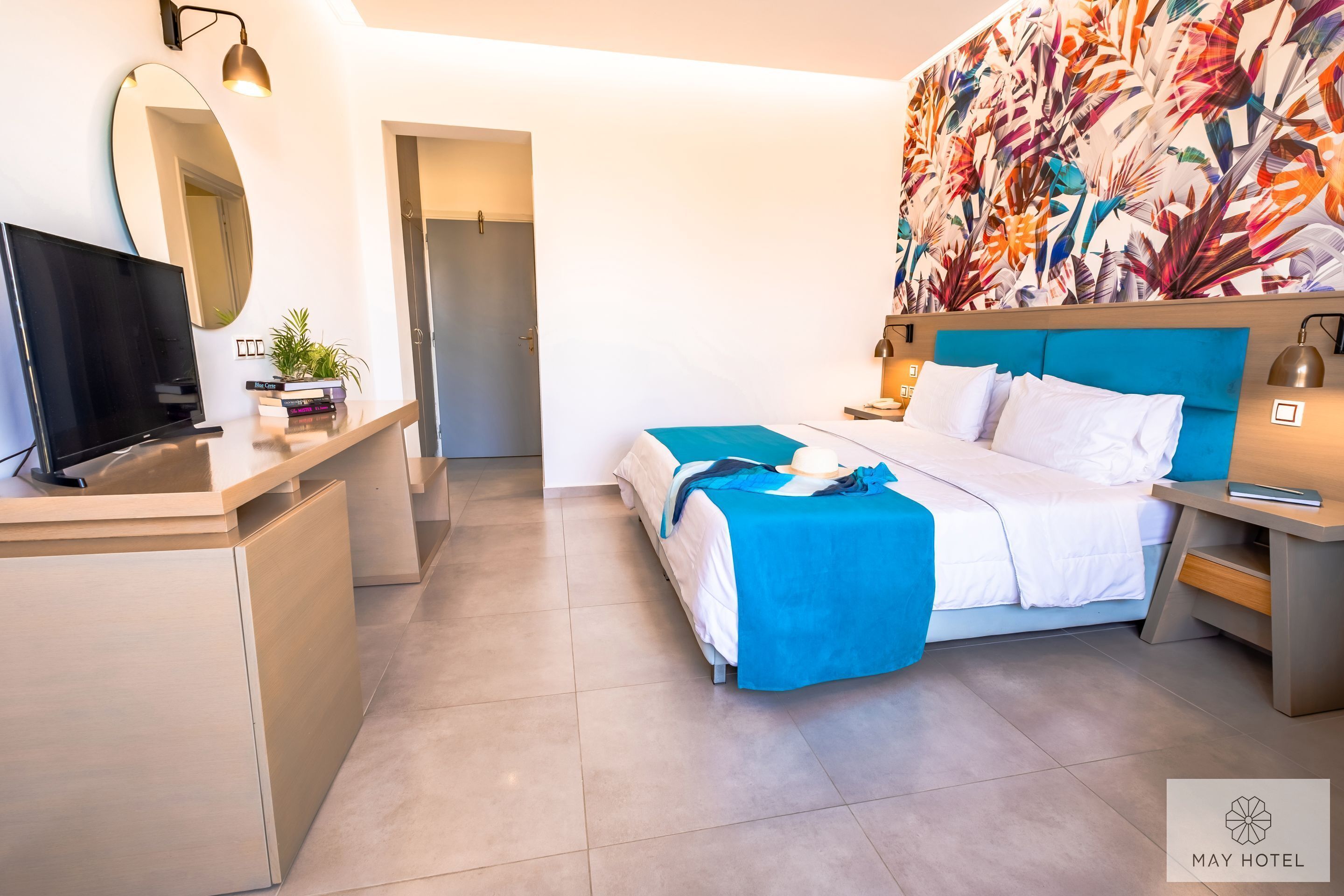 Una habitación de hotel moderna con una cama, mesitas de noche, un televisor y un gran papel tapiz tropical.