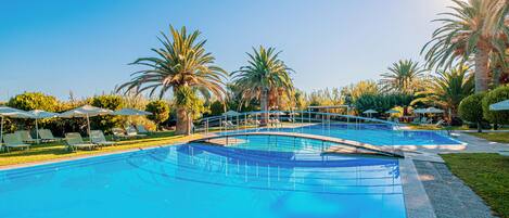 Ein großer, bogenförmiger Pool im Freien, umgeben von Palmen und Liegestühlen.