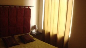 A bed with a yellow bedspread and two pillows, a nightstand with a lamp, and a window with curtains. - Hotel La Maillane (Marseille)