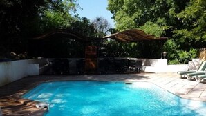 A rectangular swimming pool with a tiled deck, surrounded by lounge chairs and a covered seating area. - Hotel La Maillane (Marseille)