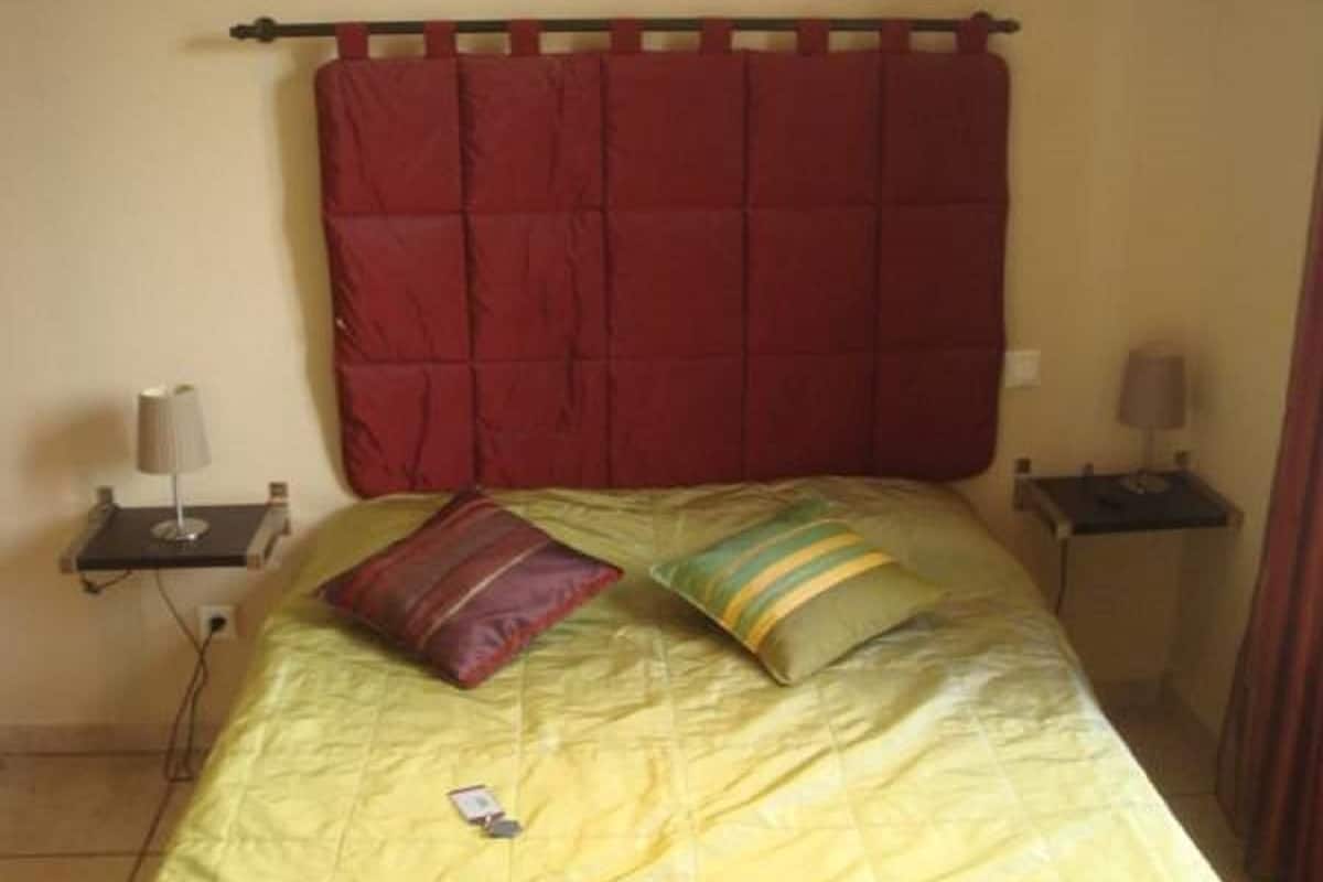 A bed with a yellow quilt, two pillows, and a red headboard. There are two bedside tables with lamps.