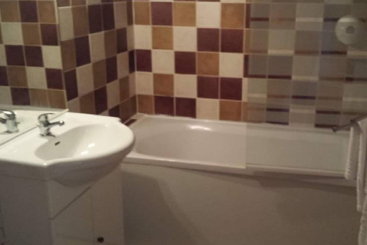 A bathroom with a white sink, a bathtub, and a tiled wall.