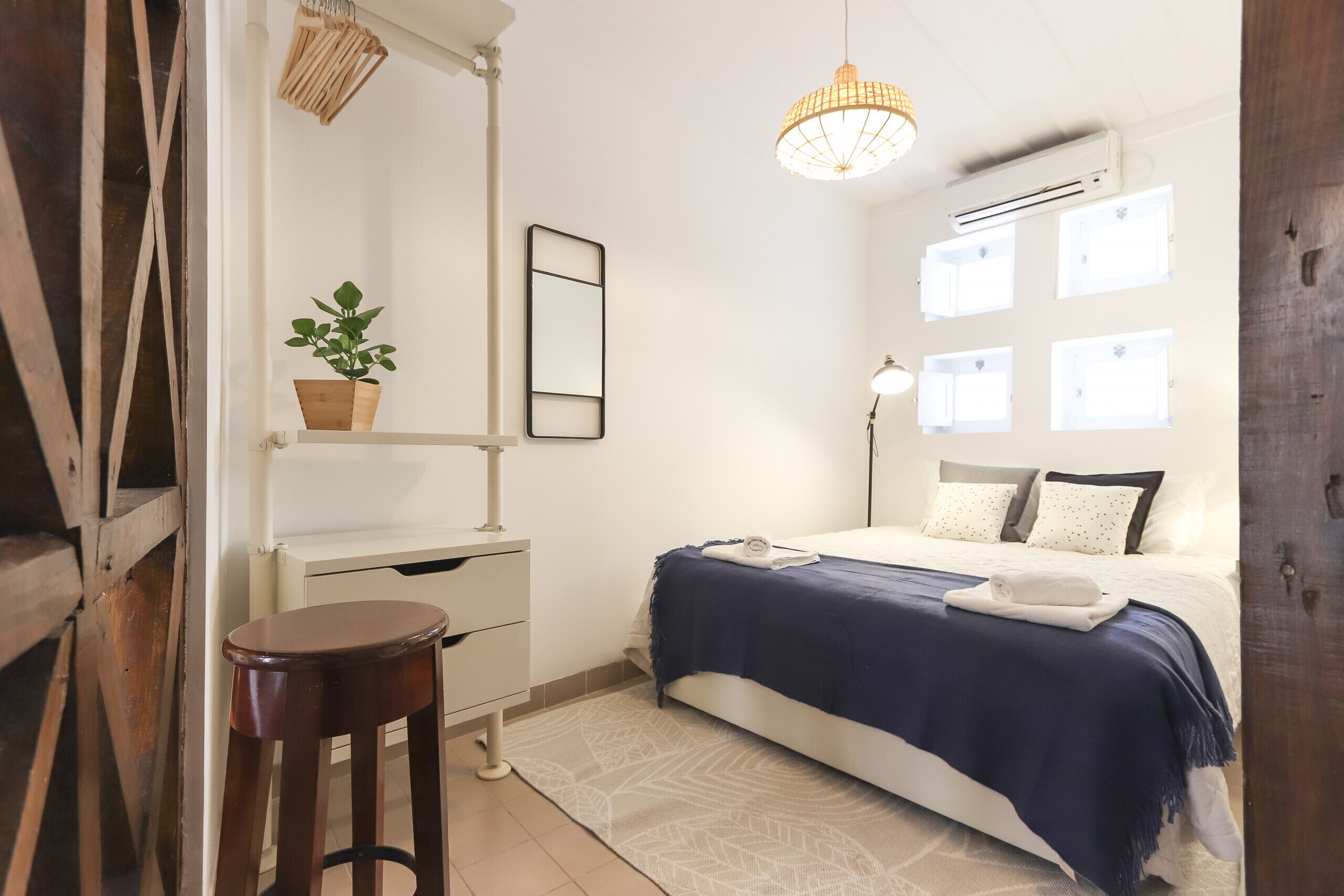 Ein Schlafzimmer mit Bett, Nachttisch, Sessel, Topfpflanze, Pendelleuchte und Fenster.