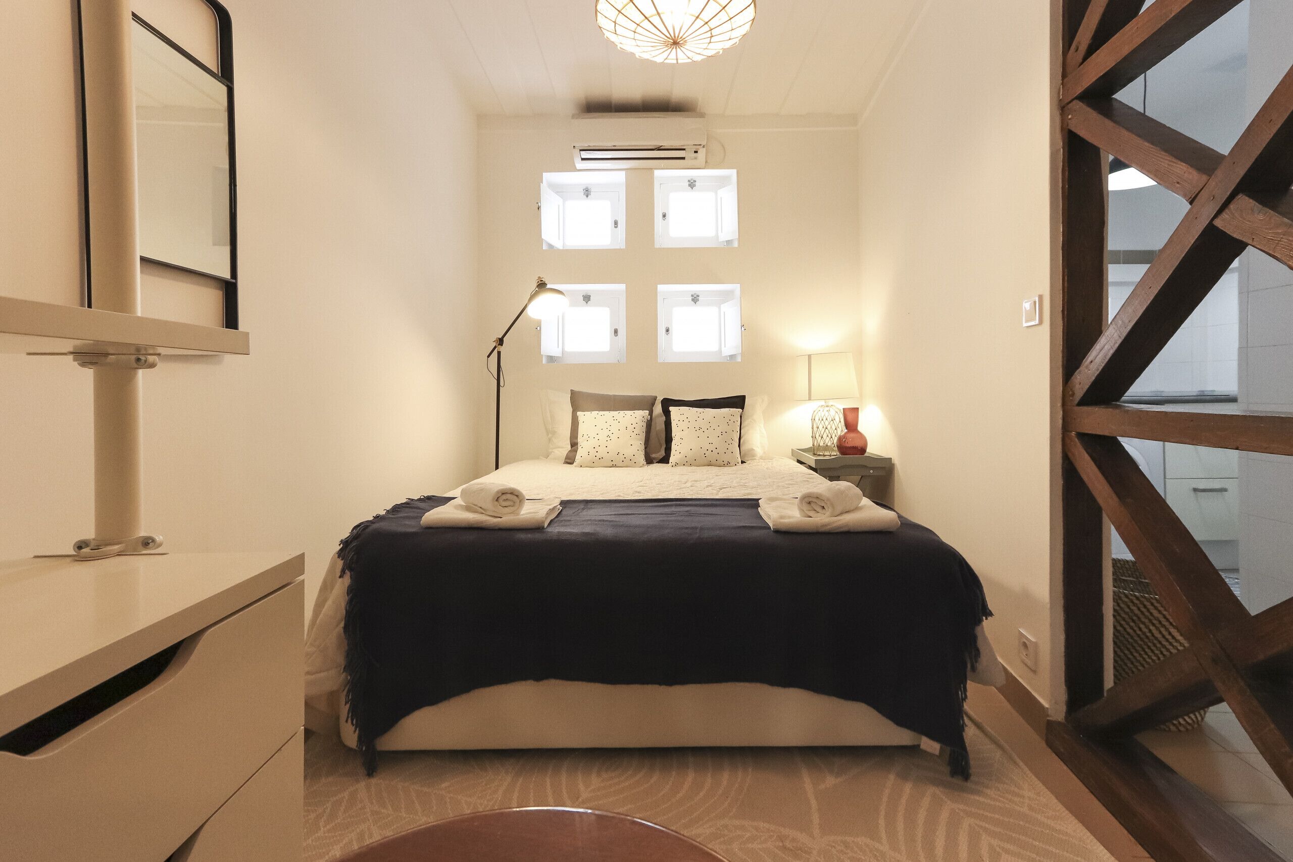 A bedroom with a bed, bedside tables, a mirror, and a window with multiple panes.