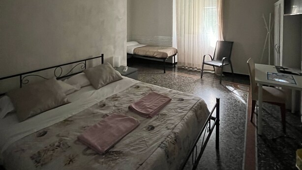 A hotel room with a bed, a desk, a chair, a window with curtains, and a painting on the wall.