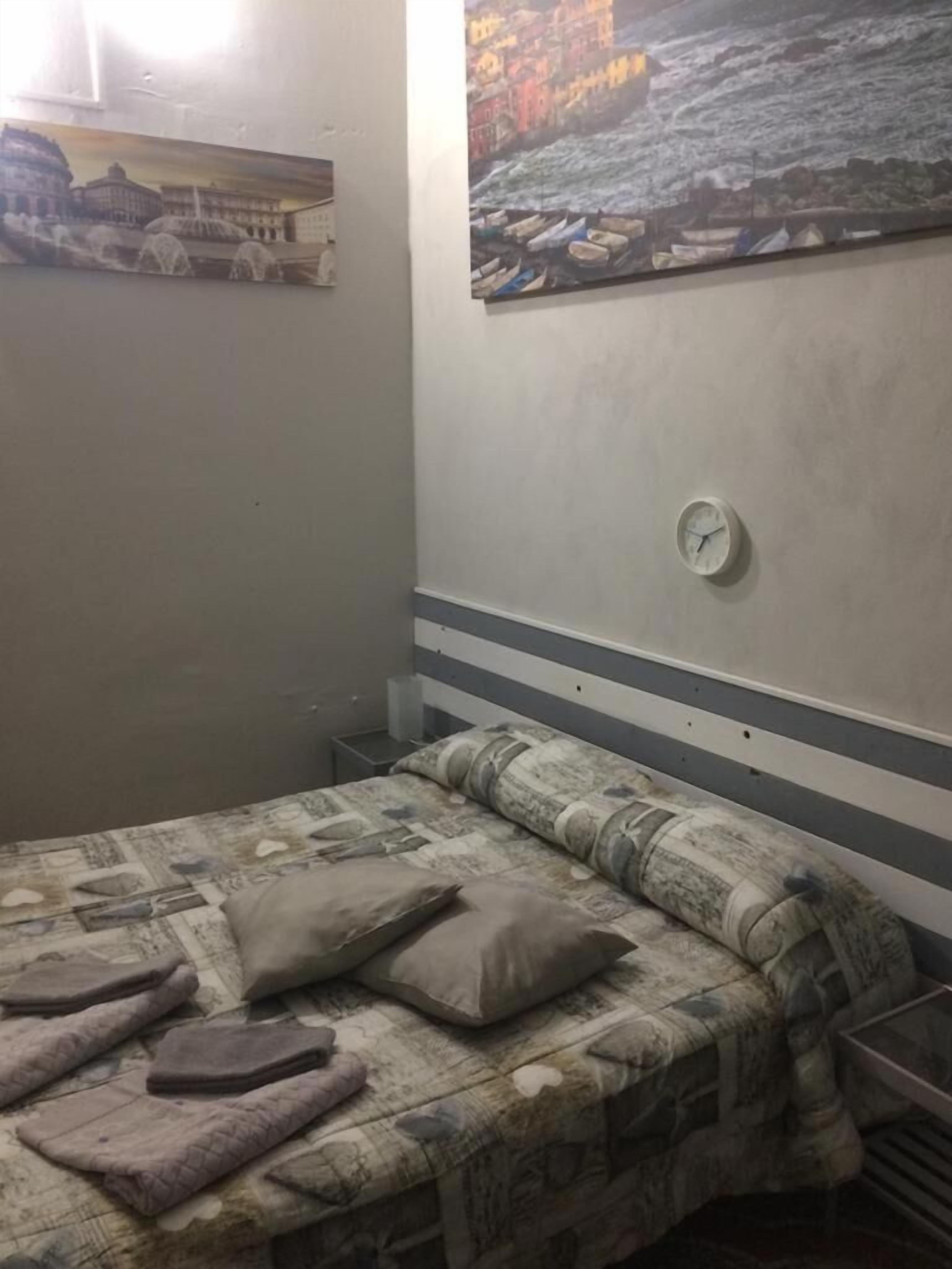 Quarto com cama, almofadas, relógio e duas pinturas na parede.
