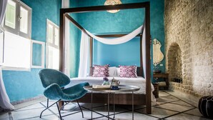 Un lit à baldaquin avec des piliers aux quatre coins, un ciel de lit blanc, un mur de couleur turquoise et un mur en pierre.
