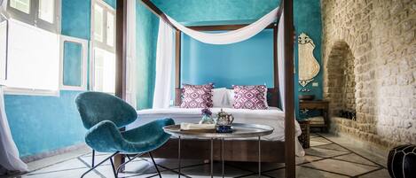 A four-poster bed with a white canopy, a teal wall, and a stone wall.