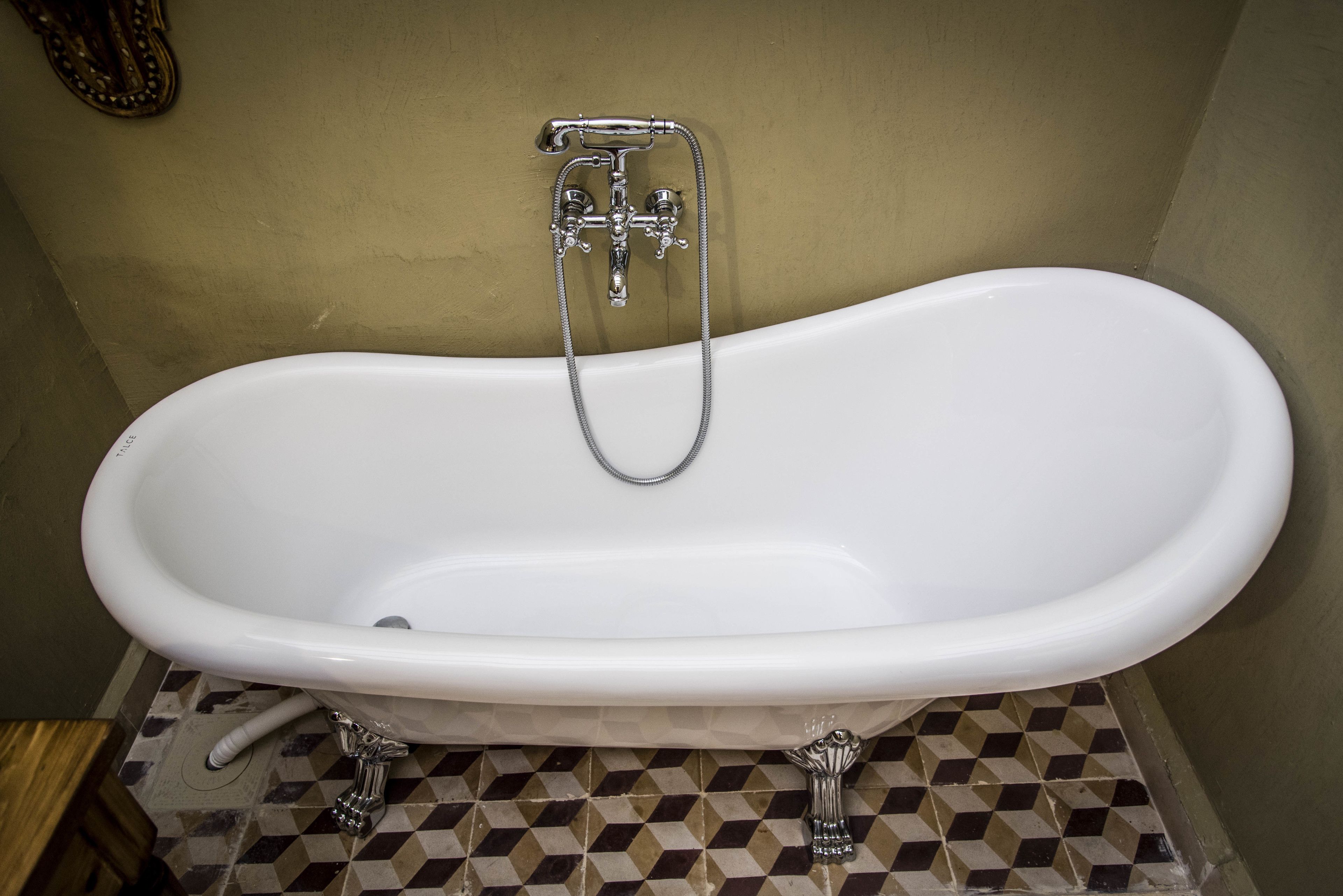A white freestanding bathtub with a shower head and hose, set on a checkered tile floor.