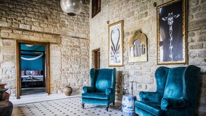 Une pièce avec un mur en pierre, deux fauteuils turquoise, un sol à motifs et un tableau représentant une girafe.