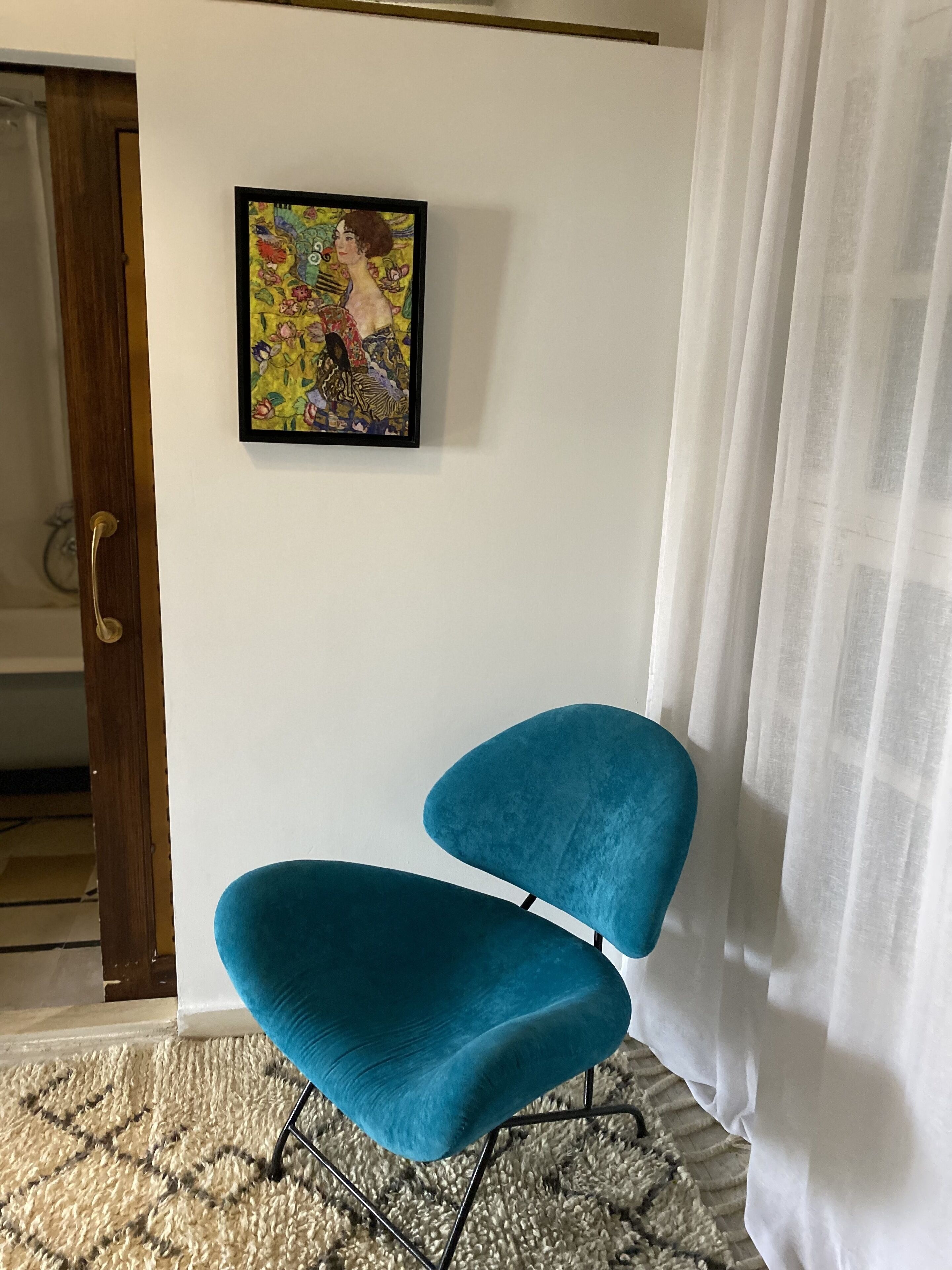 A teal chair in a room with a white wall and a framed painting.