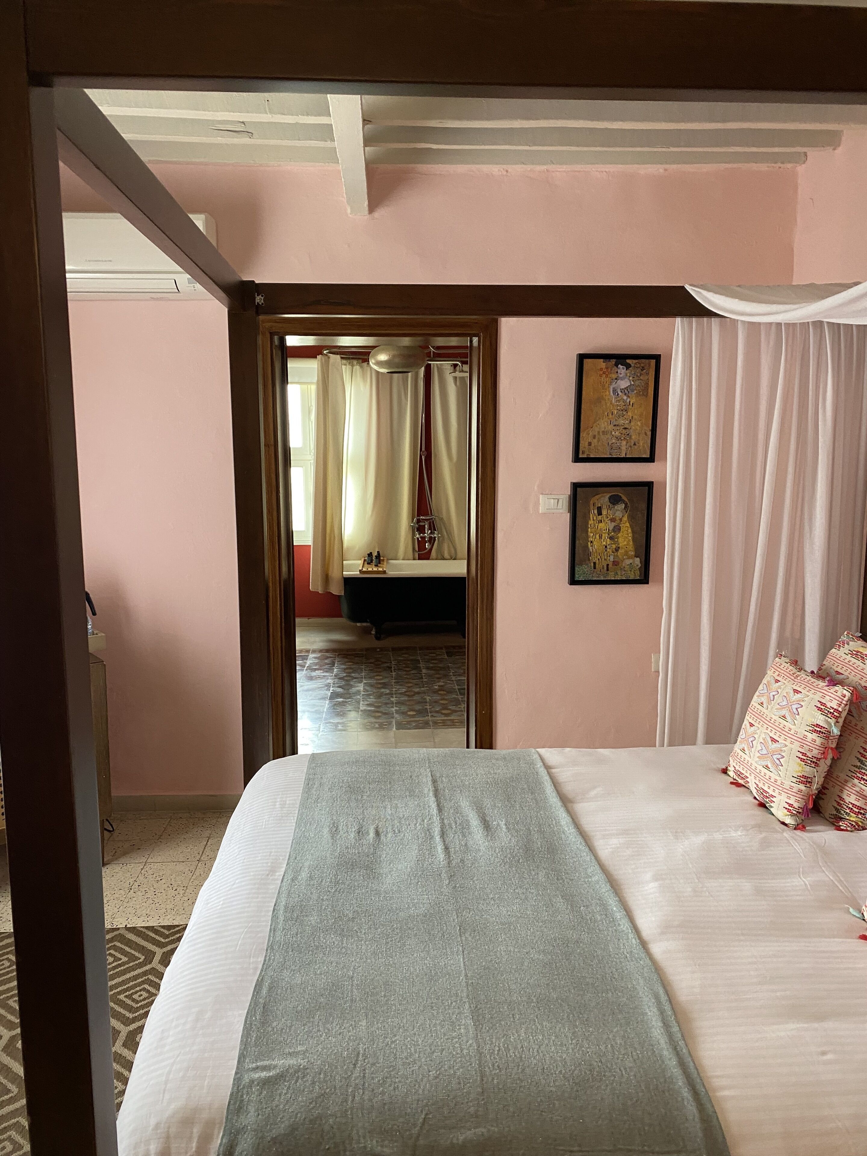 A hotel room with a bed, a bathroom visible through an open door, and two framed artworks on the wall.