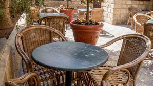 Un espace extérieur aménagé avec des chaises en osier et une table ronde, entouré de plantes en pot et d’un bâtiment en pierre.