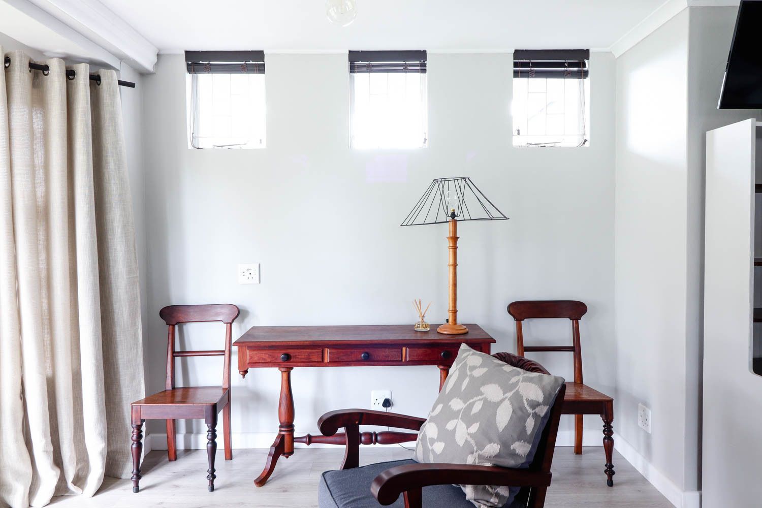 A room with a wooden desk, two chairs, a lamp, and a window with blinds.