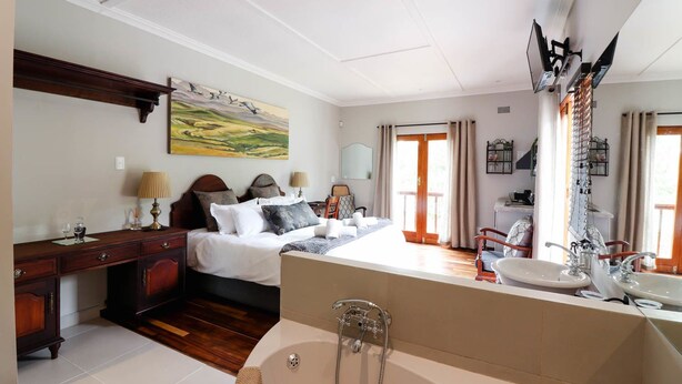A hotel room with a bed, bedside table, lamp, and a large mirror. - Arbour1 (George)