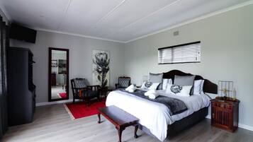 A bedroom with a large bed, a wooden bench, a red rug, a painting, and a television.