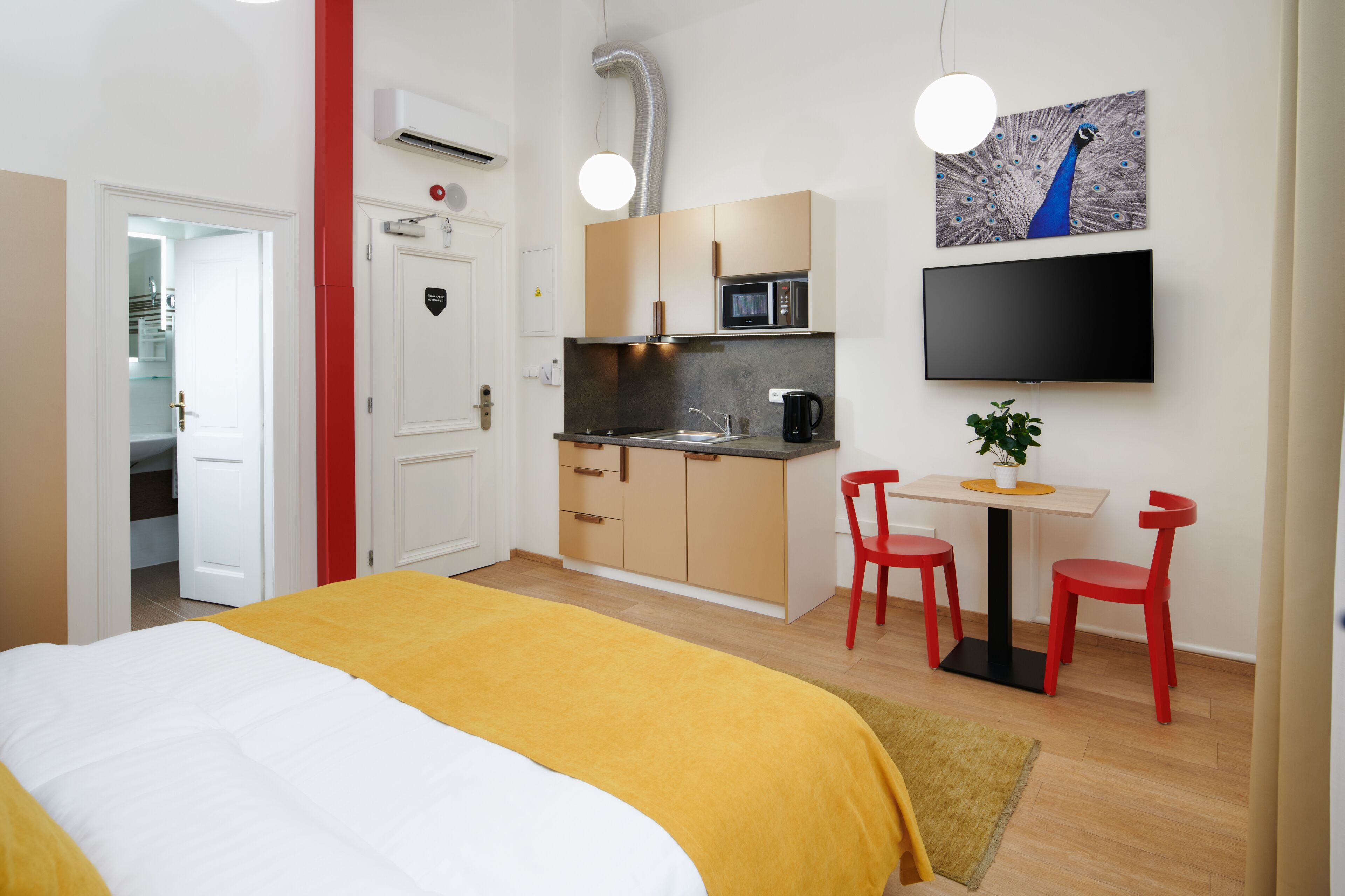 Een kleine hotelkamer met een bed, kitchenette en televisie.