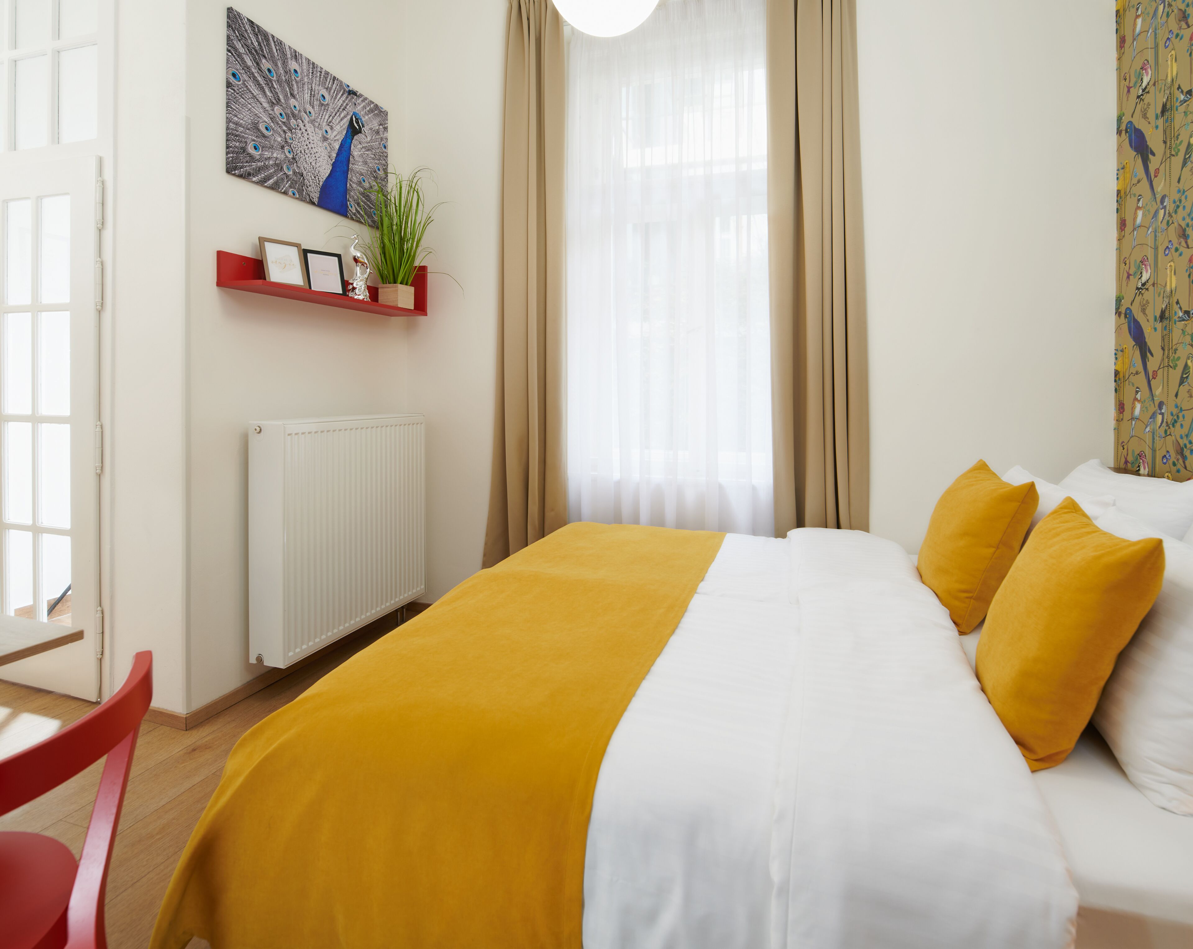 Ein Hotelzimmer mit einem Bett, einem roten Sessel, einem weißen Heizkörper, einem Regal mit Dekoration und einem Fenster mit Vorhängen.