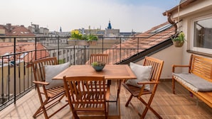 Une table et des chaises en bois sur un balcon avec vue sur la ville, des plantes en pot et un banc.