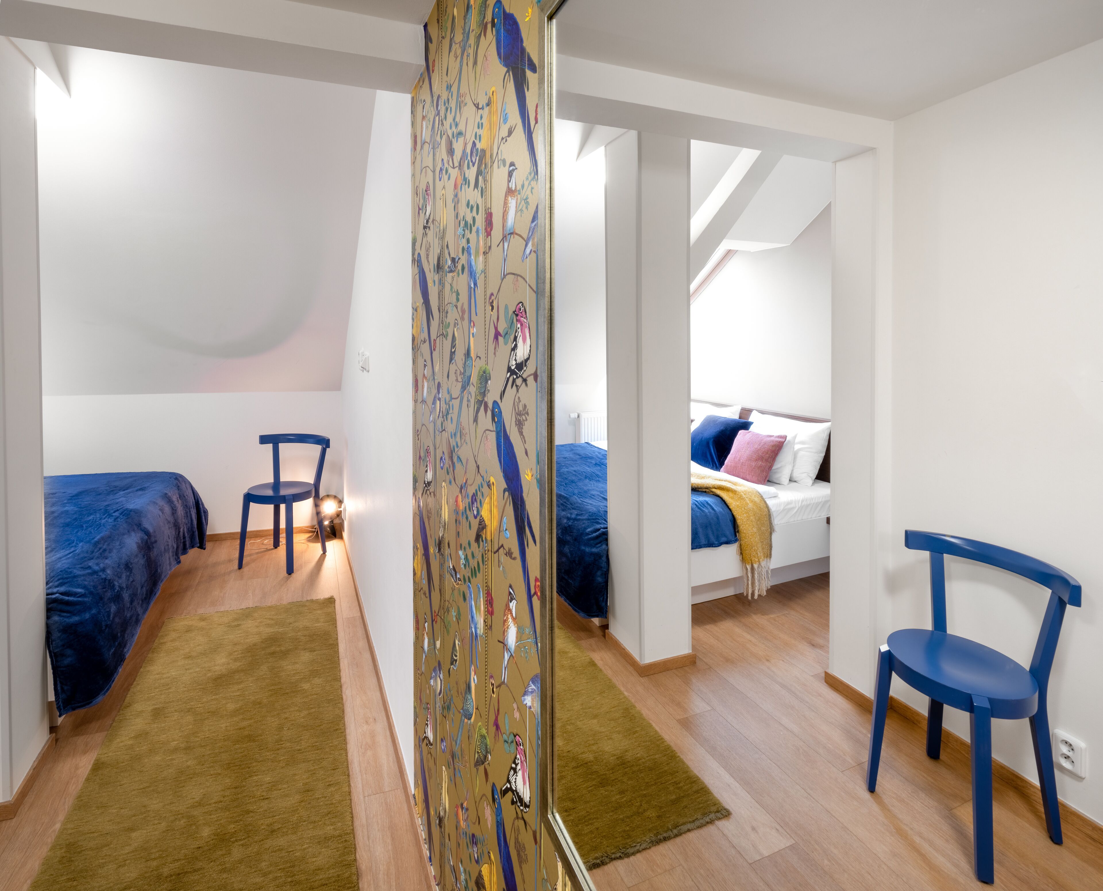 Een slaapkamer met twee bedden, een stoel en een muur met een vogelmuurschildering.