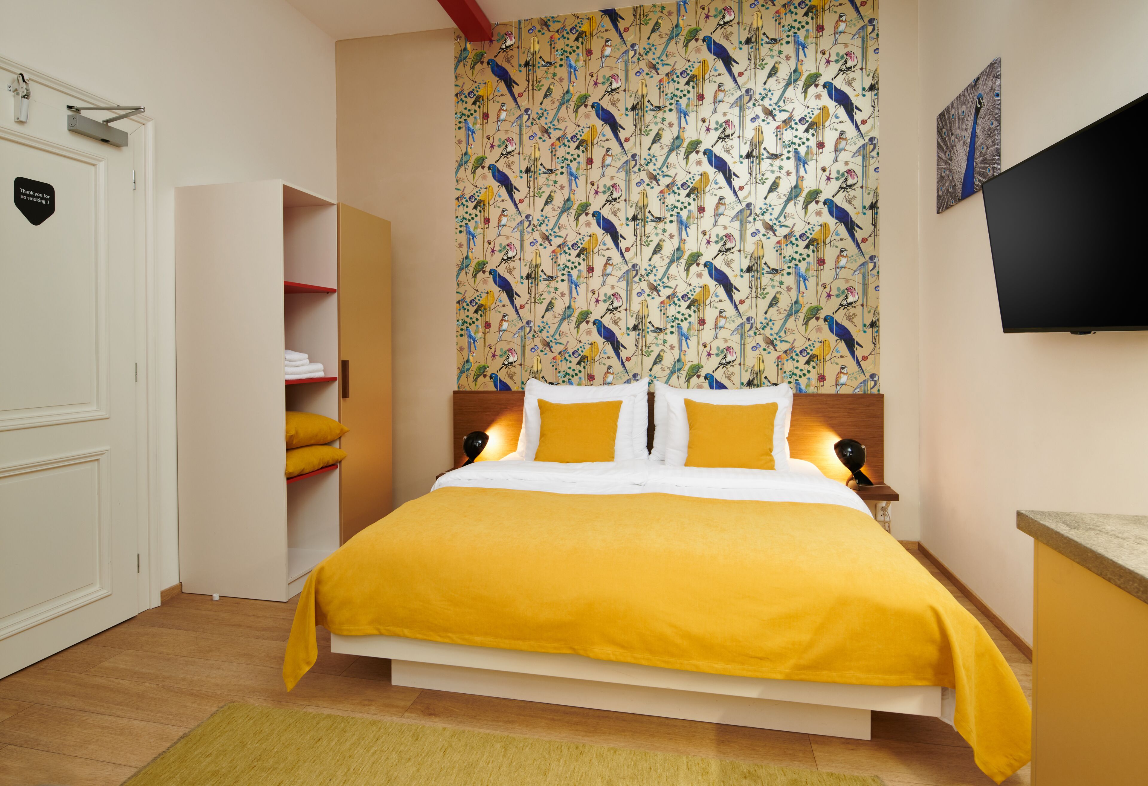 A bedroom with a bed, a wardrobe, a television, and a wall with a bird pattern.
