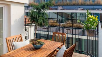 A wooden table with chairs, a potted plant, and a balcony railing.