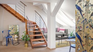 Un espace de vie de style industriel, avec un escalier en bois, un canapé, une table basse et une grande fenêtre.