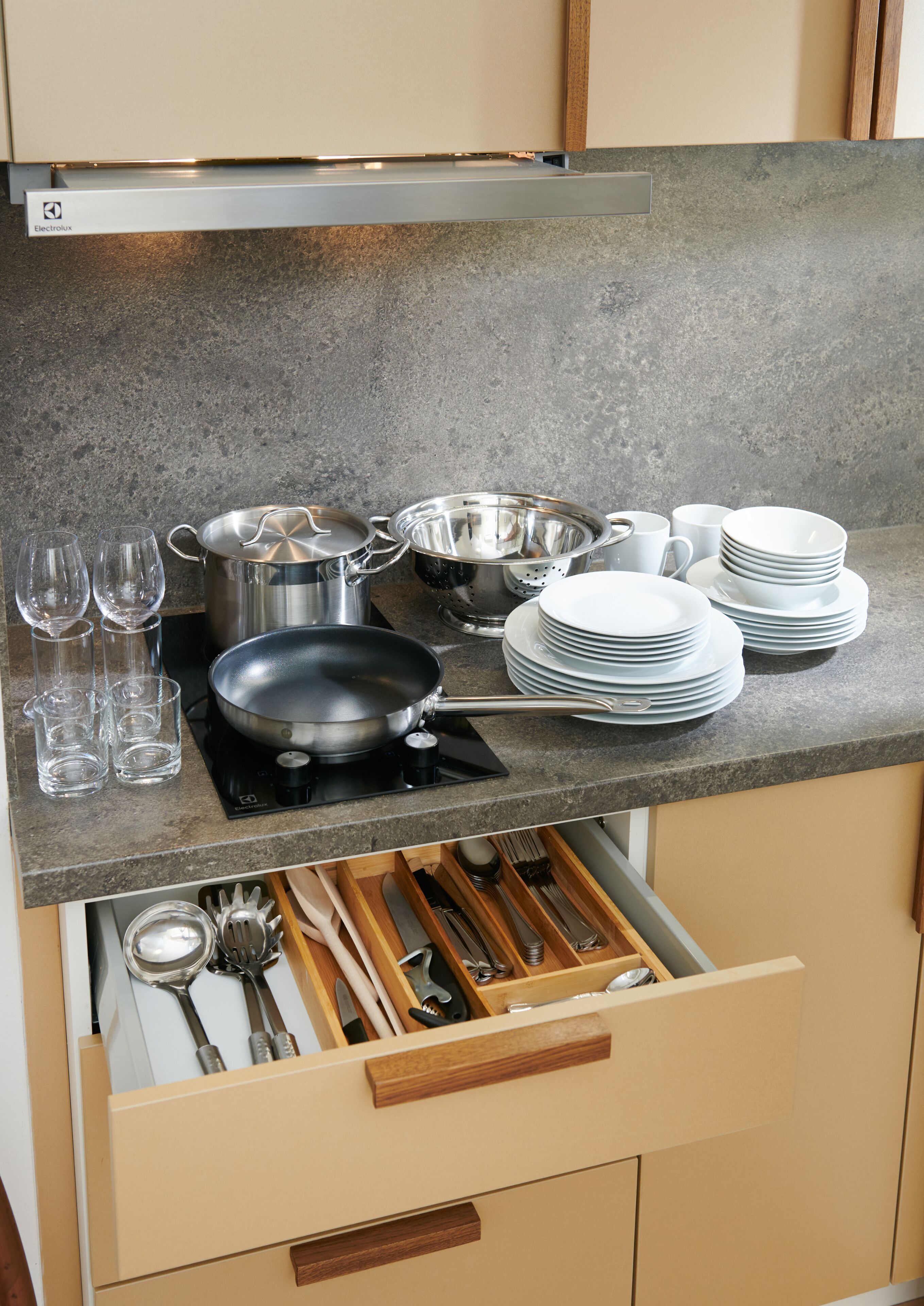 Una cocina con encimera gris, utensilios de cocina de acero inoxidable, platos blancos y vasos.