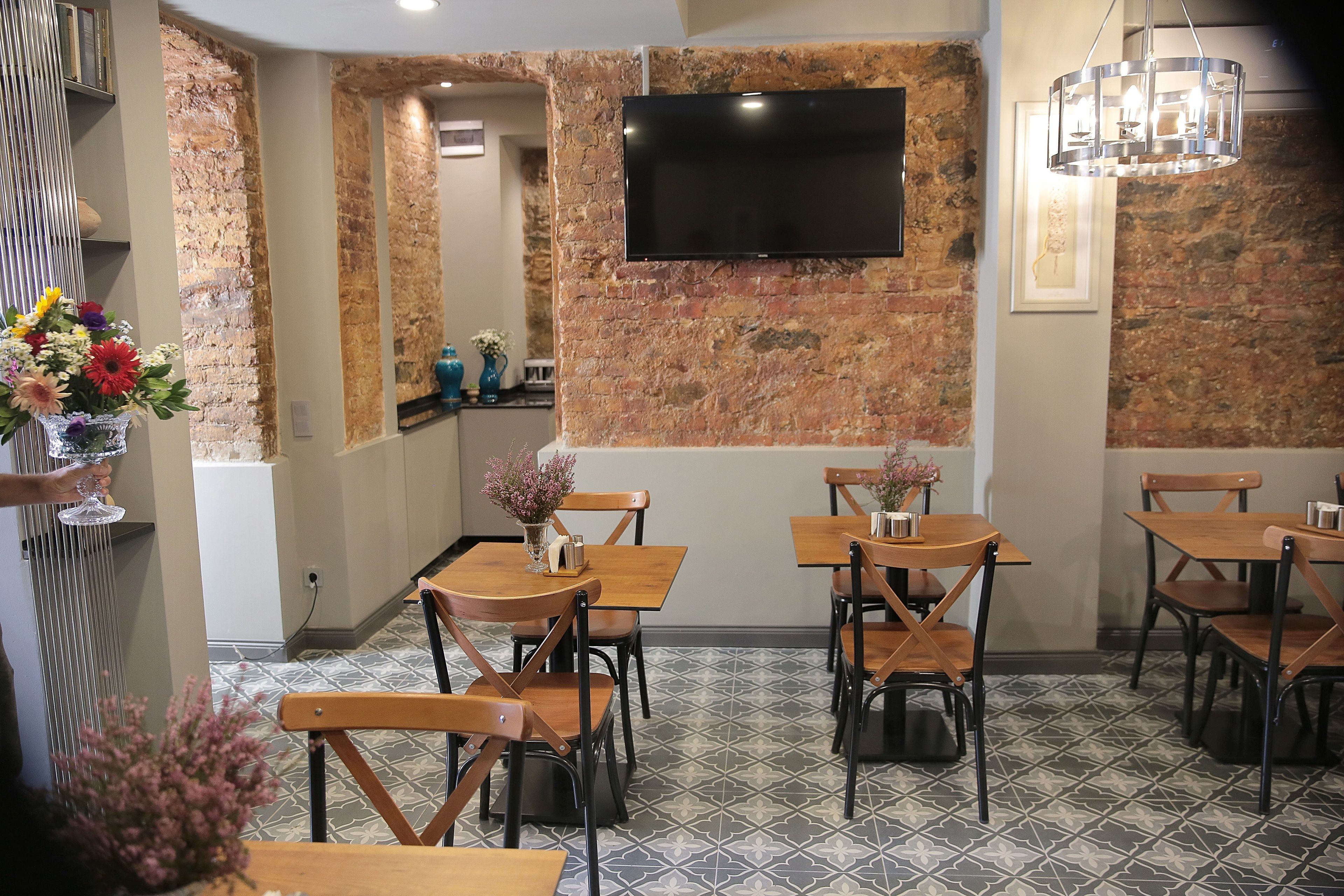 Un restaurante con paredes de ladrillo, una televisión de pantalla plana, mesas y sillas de madera y baldosas de suelo con diseños.