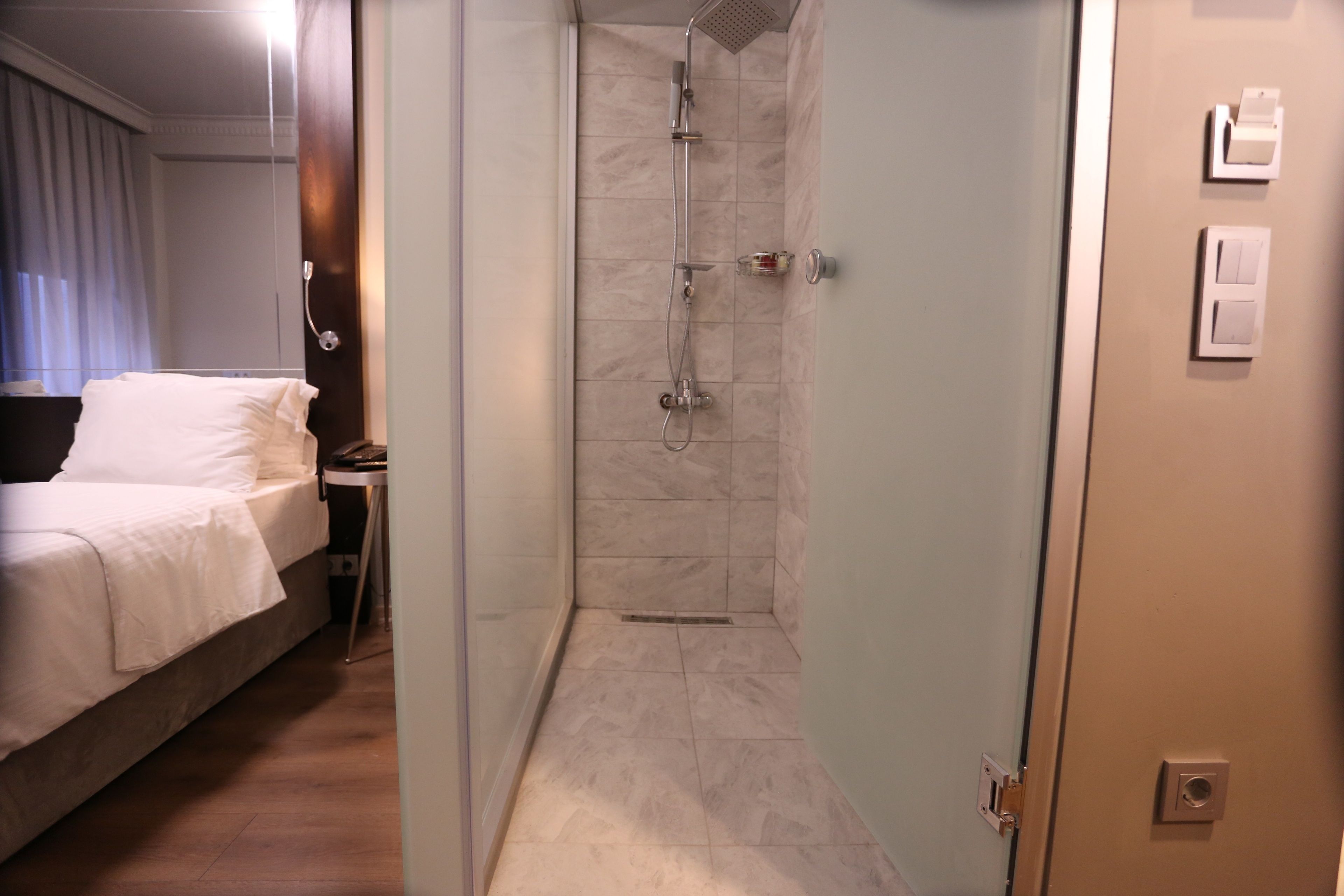 A hotel room with a bed, a shower area, and a door with a light switch.