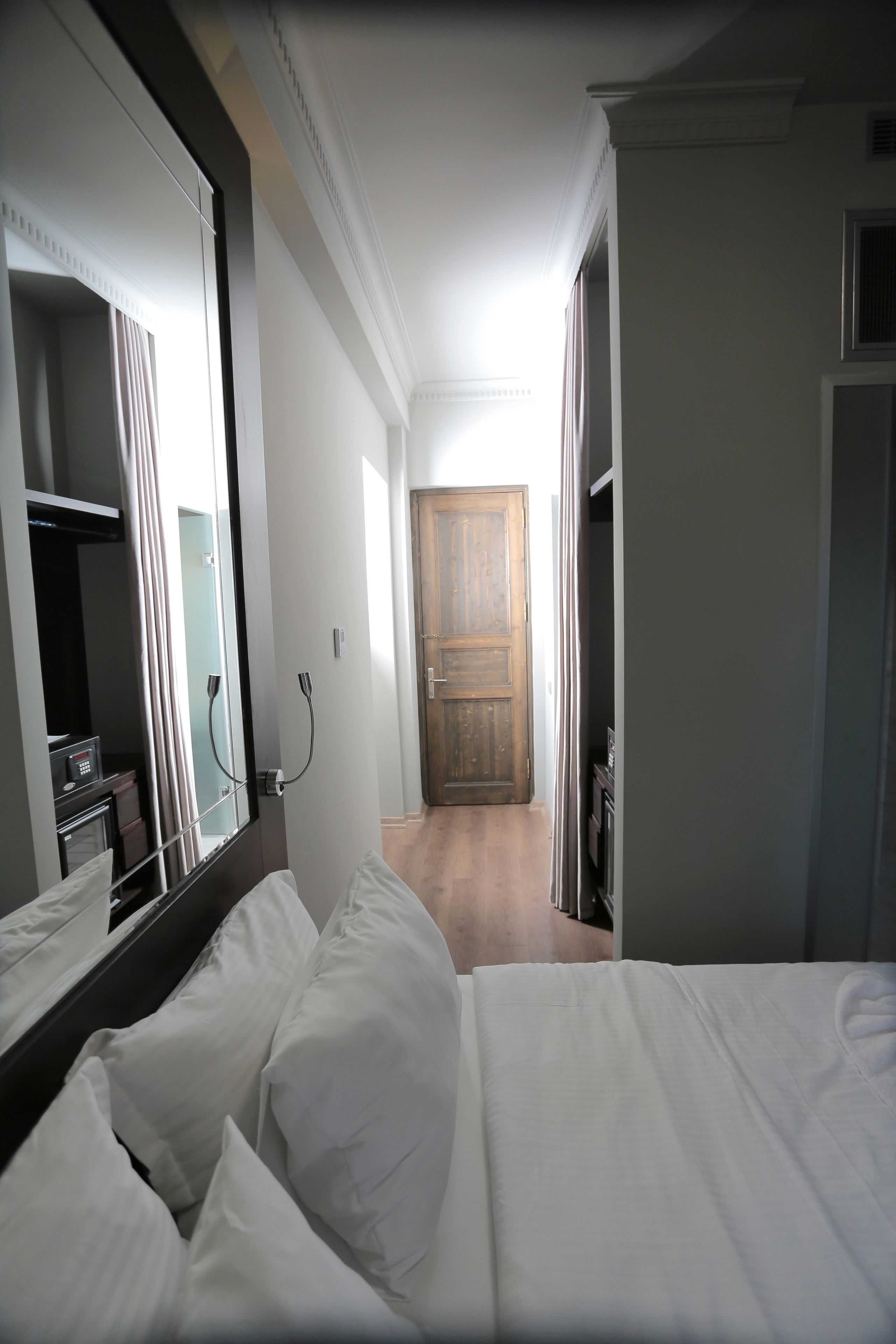 A hotel room with a bed, a large mirror, a wardrobe, and a wooden door leading to another room.