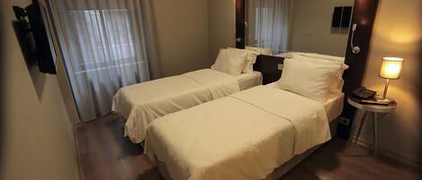 Habitación de hotel con dos camas, una mesita de noche con lámpara, un espejo y una ventana con cortinas.