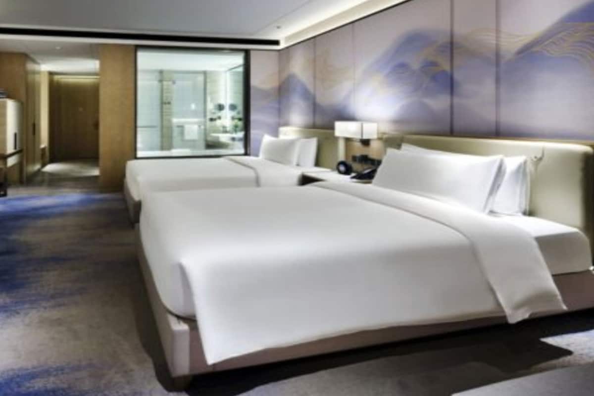 A hotel room with a large bed, a flat-screen TV mounted on the wall, and a small table with fruit.