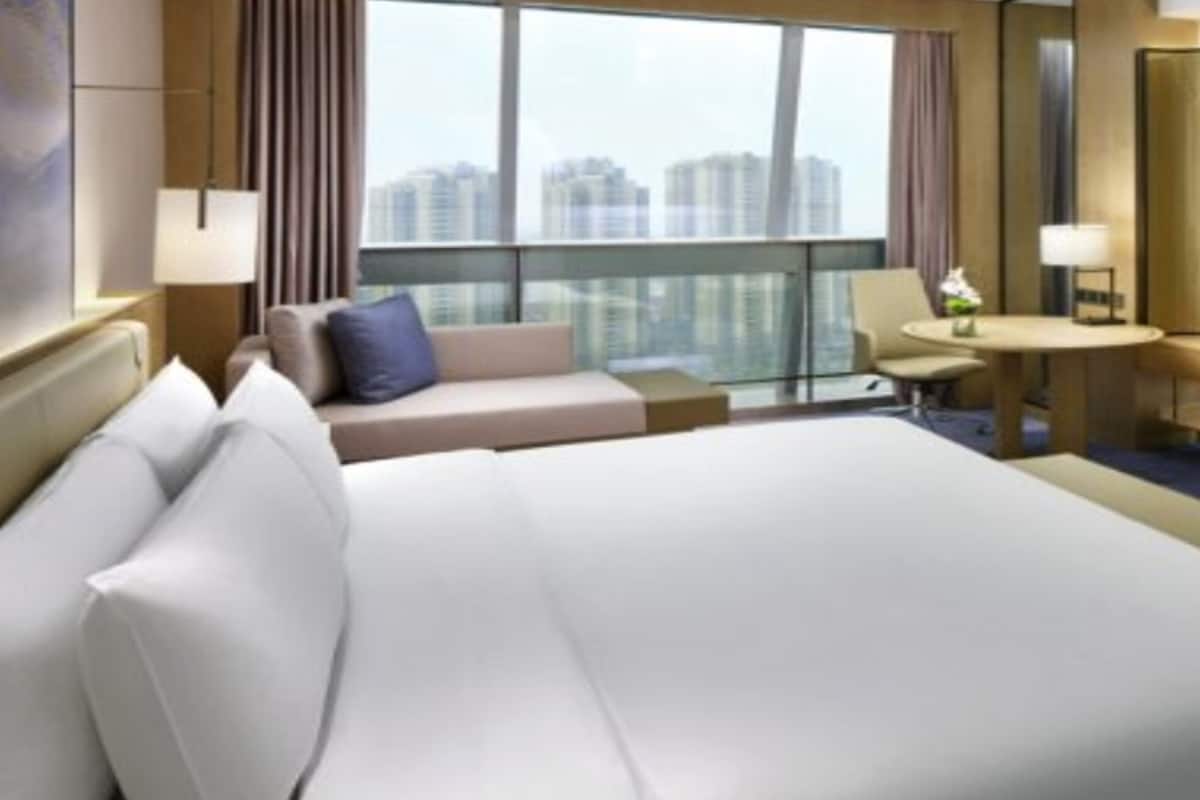 A hotel room with a large bed, a sofa, a small table, a TV, and a city view.