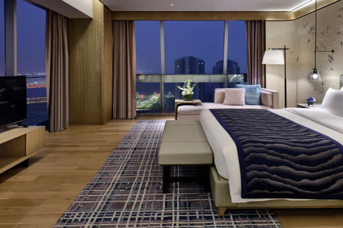 A modern hotel room with a large bed, a TV, and a view of the cityscape at night.