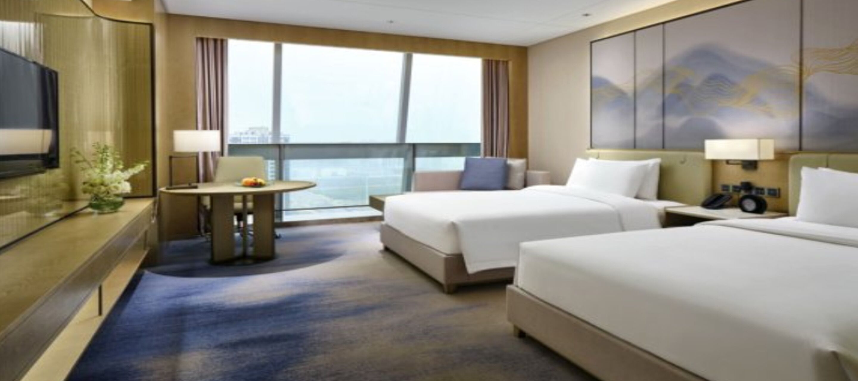 Habitación de hotel con dos camas, una mesita con lámpara, televisor y un ventanal con vistas.