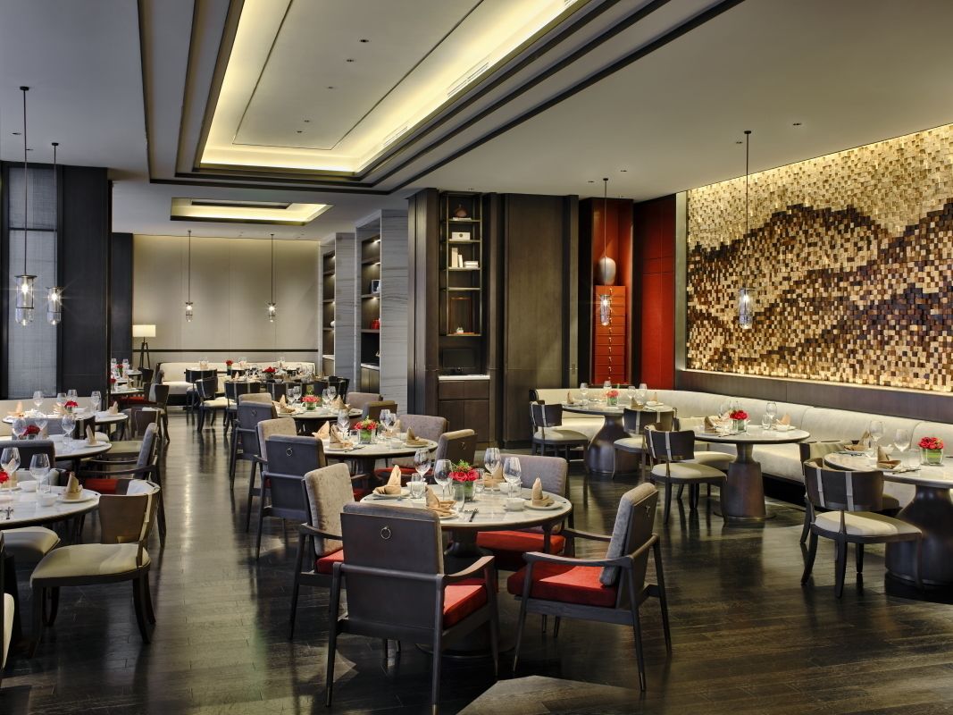 A modern restaurant with round tables and chairs, a patterned wall, and pendant lighting.