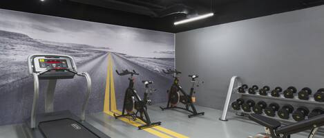 A gym with treadmills, stationary bikes, and a rack of dumbbells.