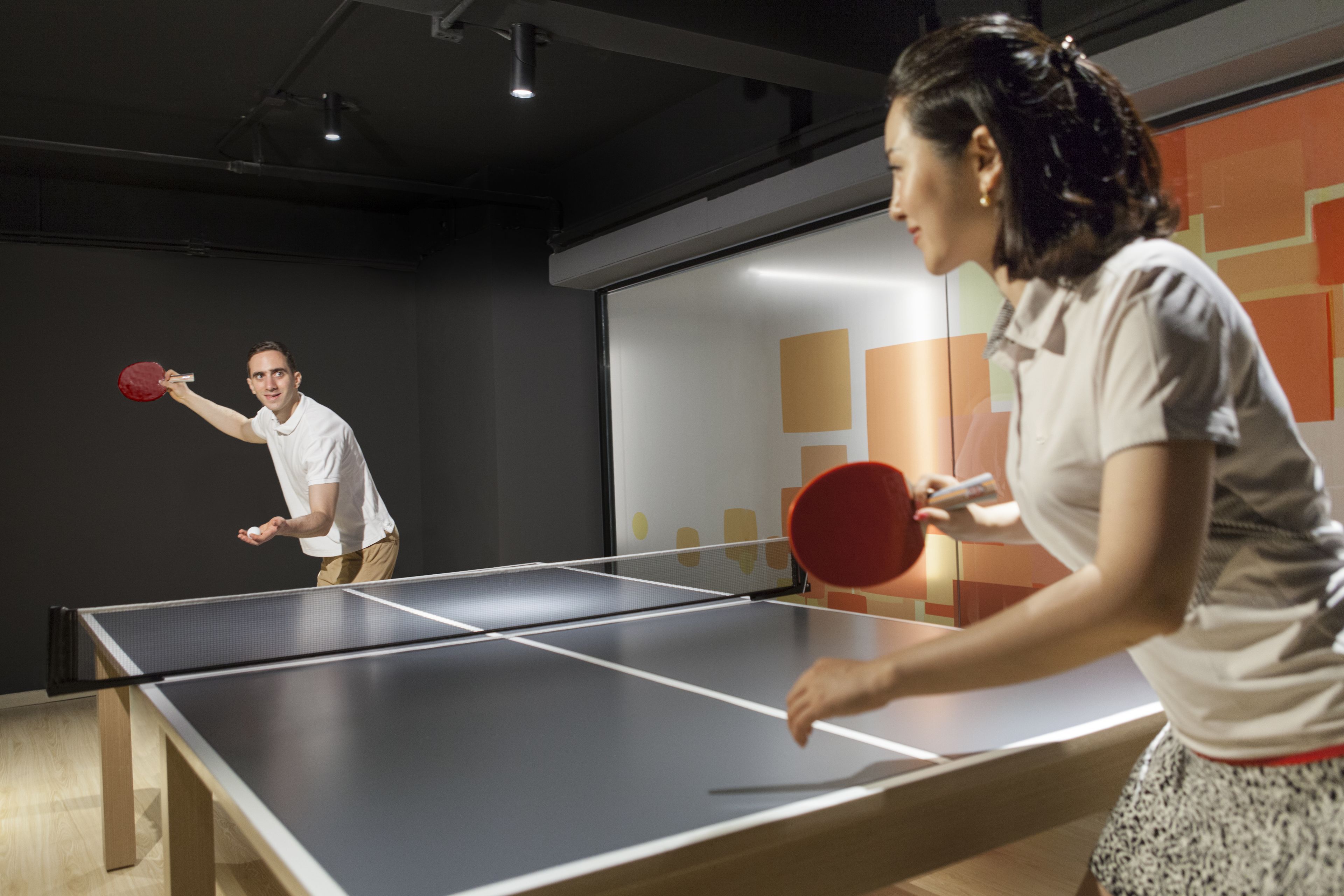 A ping pong table in a room with a modern design, including a glass partition and abstract wall art.