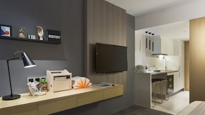 Une chambre d’hôtel moderne équipée d’un téléviseur à écran plat, d’un bureau avec une lampe, d’une petite plante et d’une étagère ornée d’objets décoratifs.