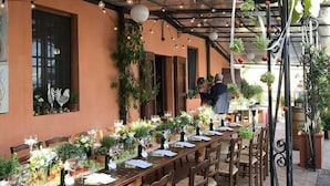 Un área de comedor al aire libre con mesas y sillas de madera, luces colgantes y plantas en macetas.